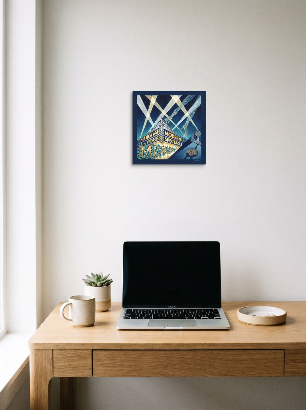A 12x12 inch canvas Art Deco print of 'The New Age Spectacle' hanging above a worktable with a laptop.