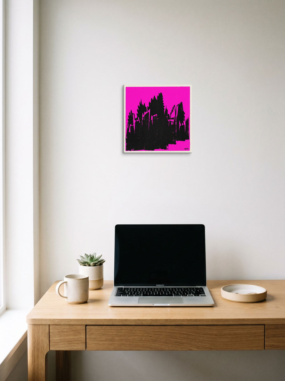 A 12x12 inch canvas Pop art print of 'Neon Urban Decay' hanging above a worktable with a laptop.