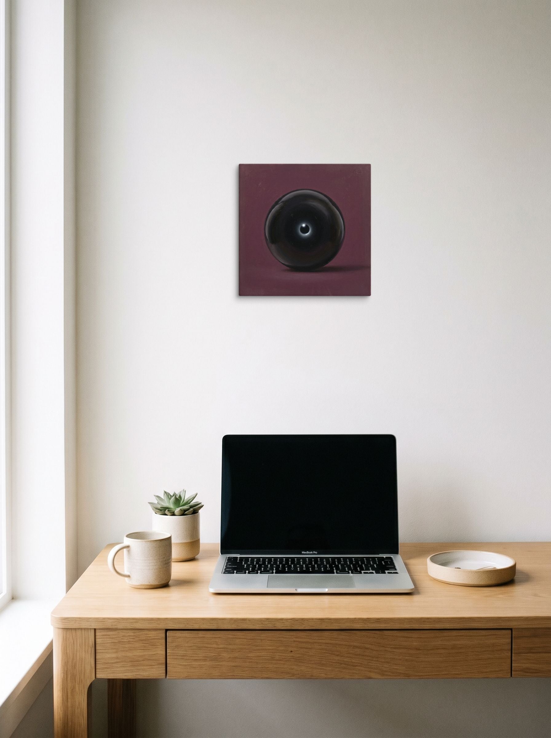 A 12x12 inch canvas Surrealism print of 'Obsidian Eye' hanging above a worktable with a laptop.