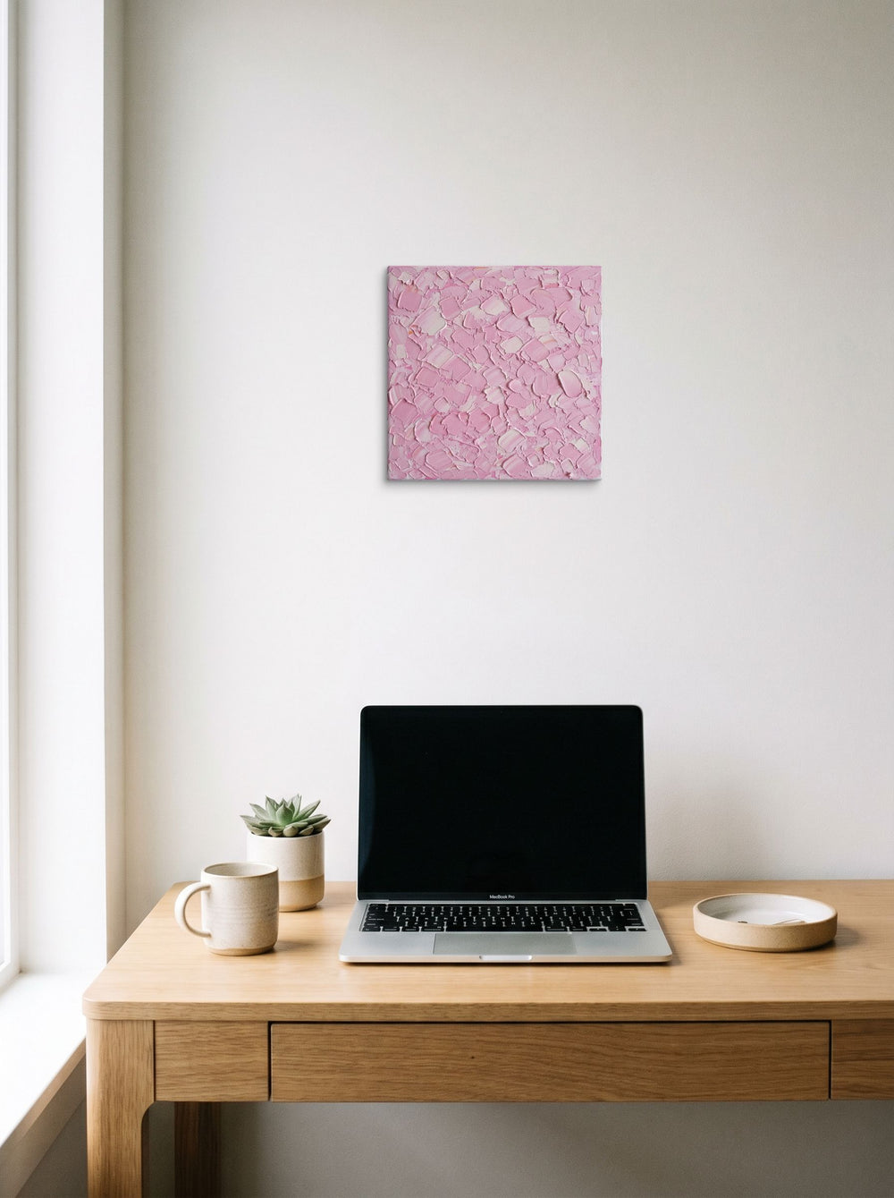 A 12x12 inch canvas Expressionism print of 'Blush Topography' hanging above a worktable with a laptop.