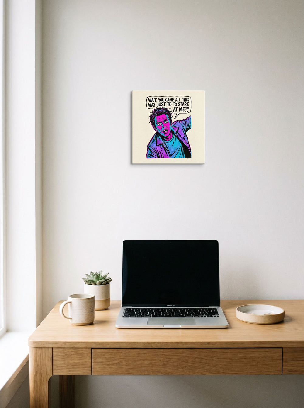 A 12x12 inch canvas Pop art print of 'The Stare Down' hanging above a worktable with a laptop.