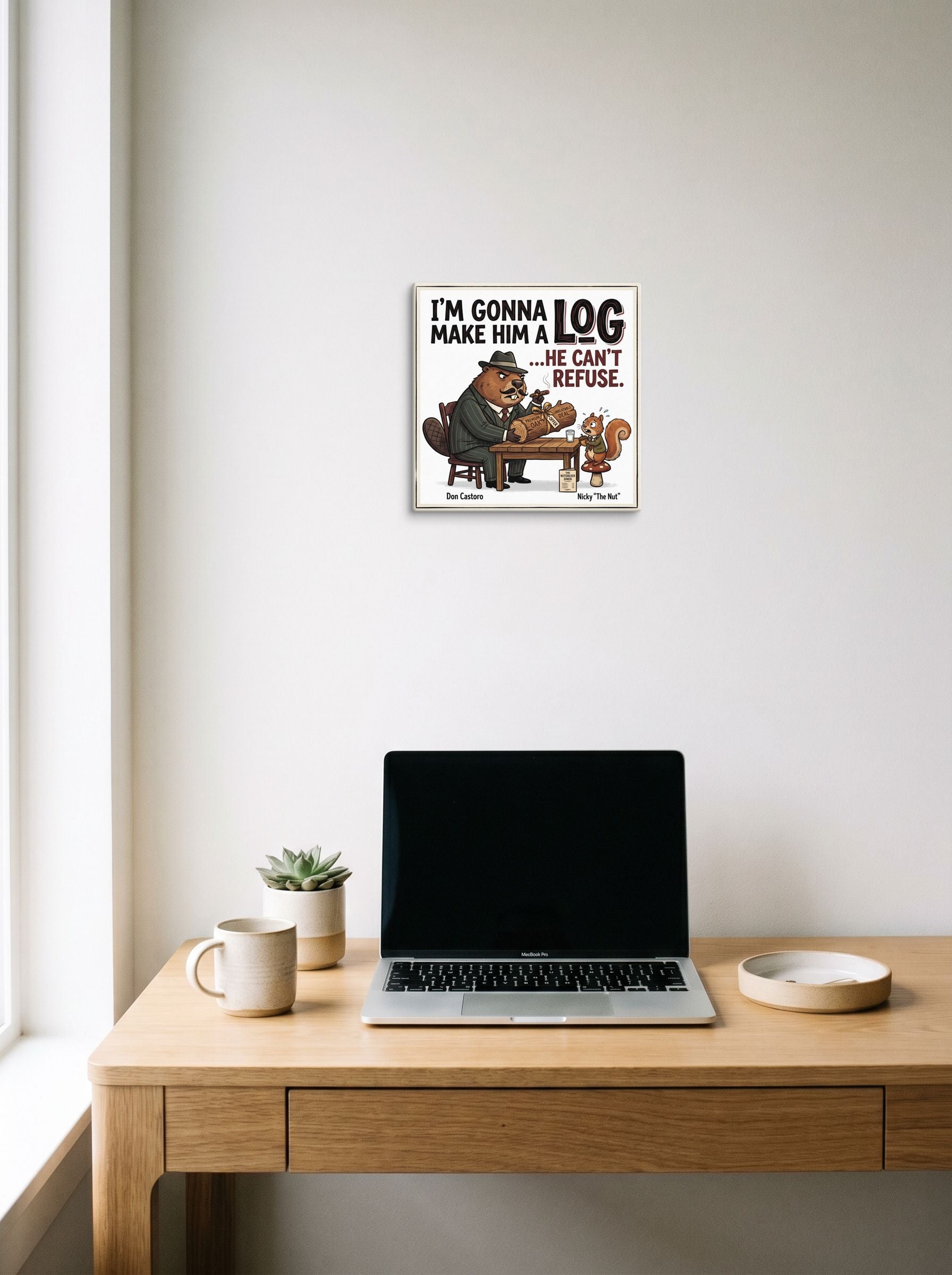 A 12x12 inch canvas Pop art print of 'Make Him a Log' hanging above a worktable with a laptop.