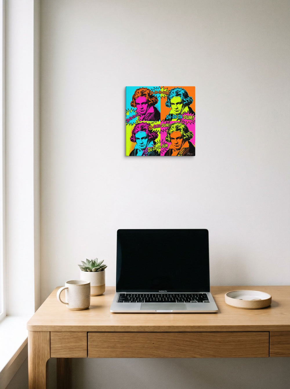A 12x12 inch canvas Pop art print of 'Beethoven in Technicolor', hanging above a worktable with a laptop.