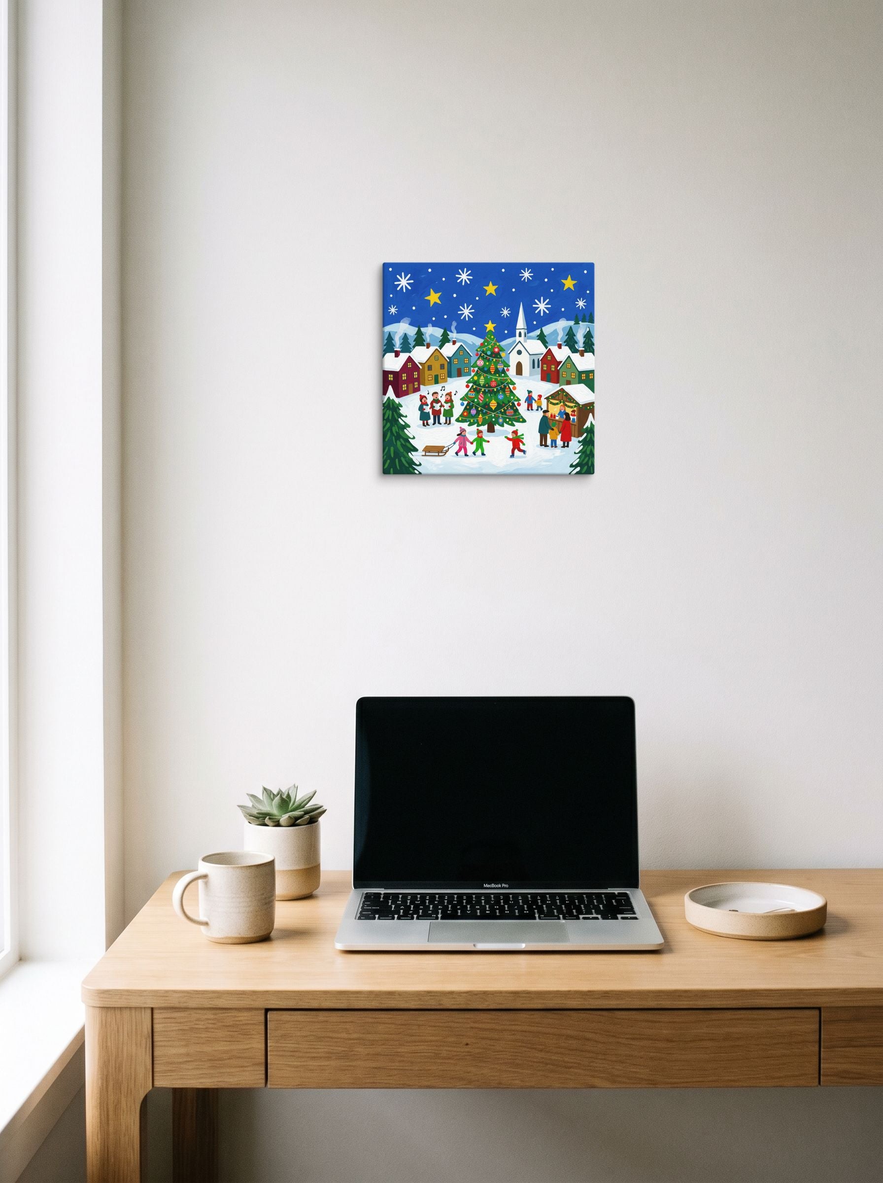 A 12x12 inch canvas Naive art print of 'Joyous Christmas Village' hanging above a worktable with a laptop.