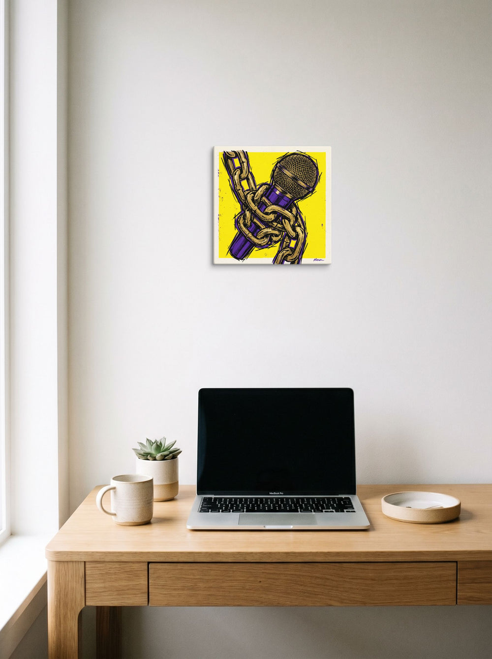 A 12x12 inch canvas Pop art print of 'Chained Mic' hanging above a worktable with a laptop.