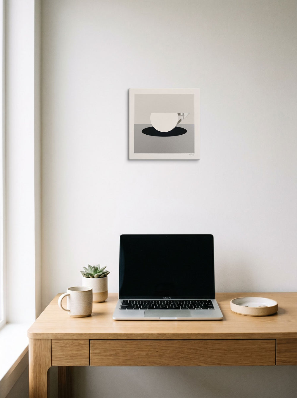A 12x12 inch canvas Art Deco print of 'The Abstract Cup' hanging above a worktable with a laptop.