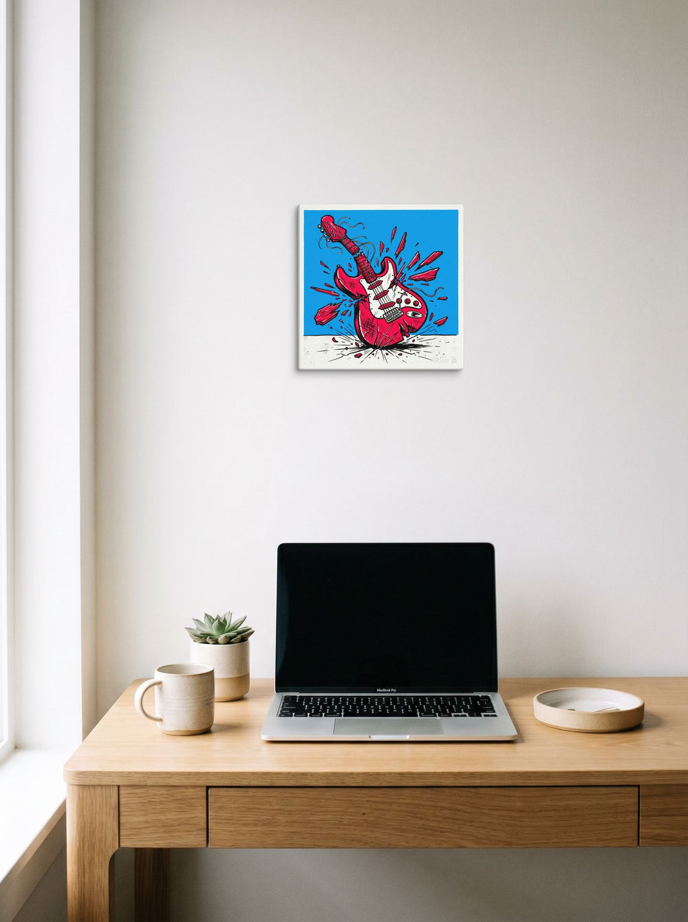 A 12x12 inch canvas Pop art print of 'Guitar Smash' hanging above a worktable with a laptop.