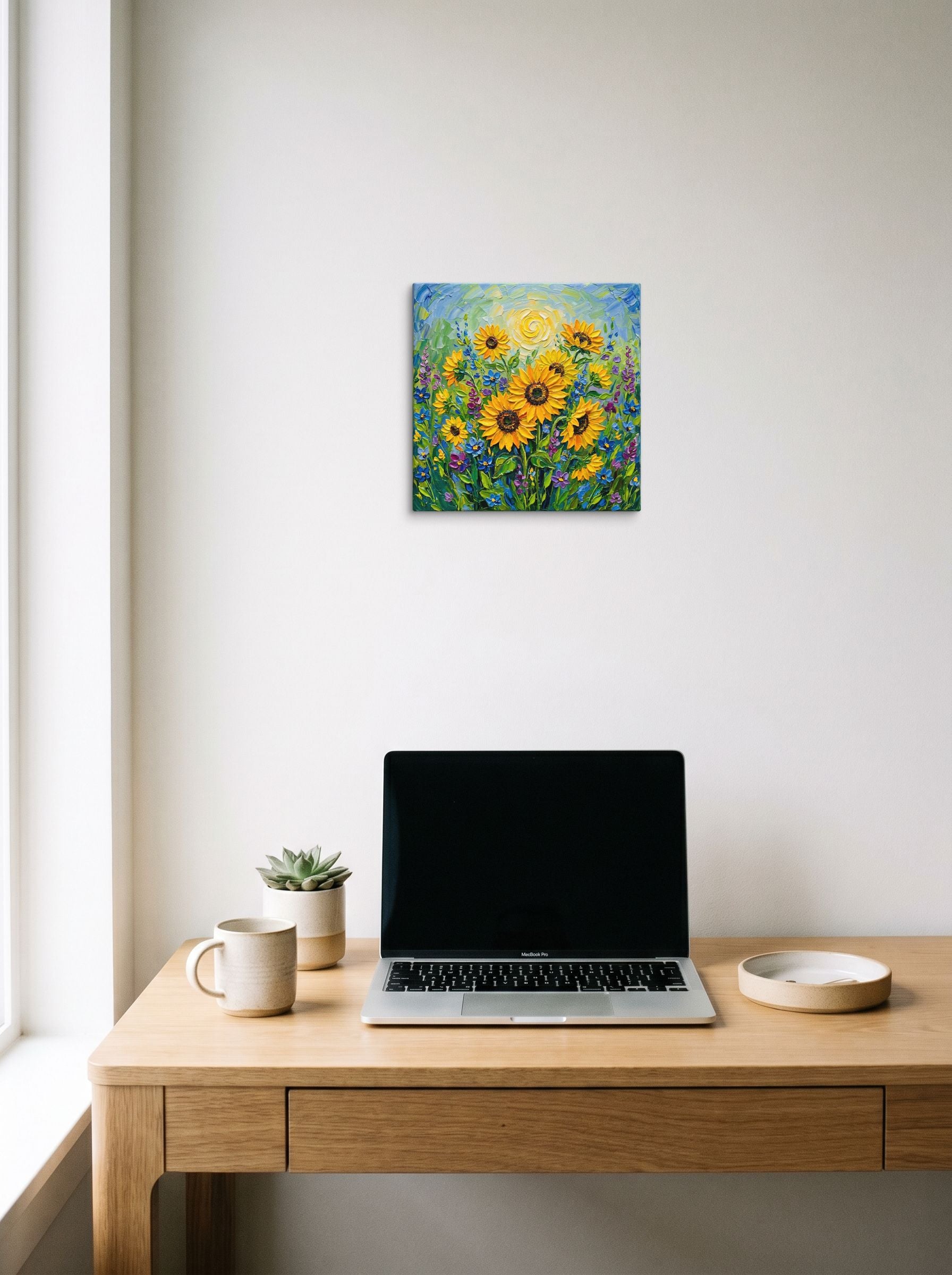 A 12x12 inch canvas Impressionism print of 'Sunlit Blooms' hanging above a worktable with a laptop.