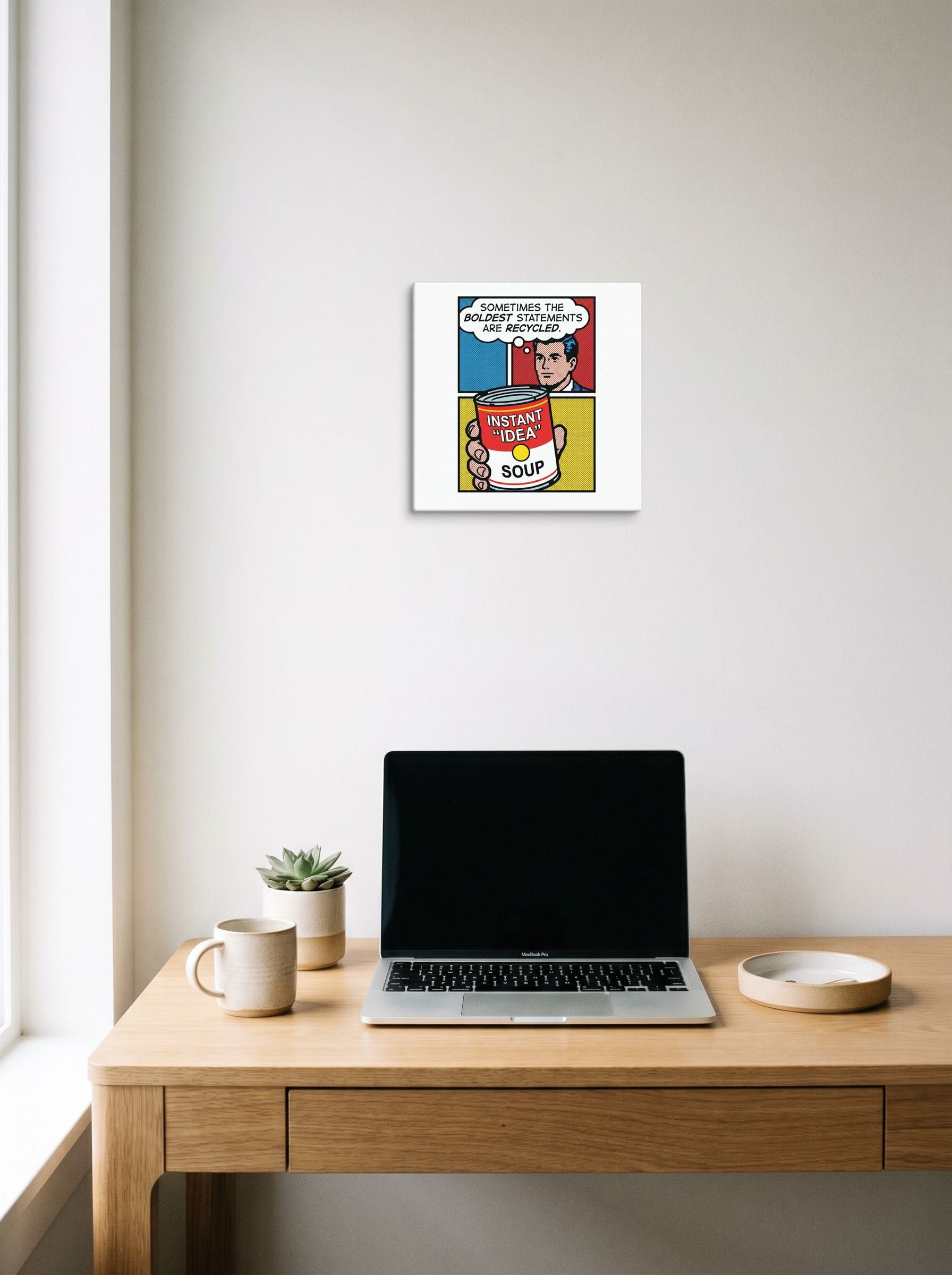 A 12x12 inch canvas Pop art print of 'Recycled Ideas' hanging above a worktable with a laptop.