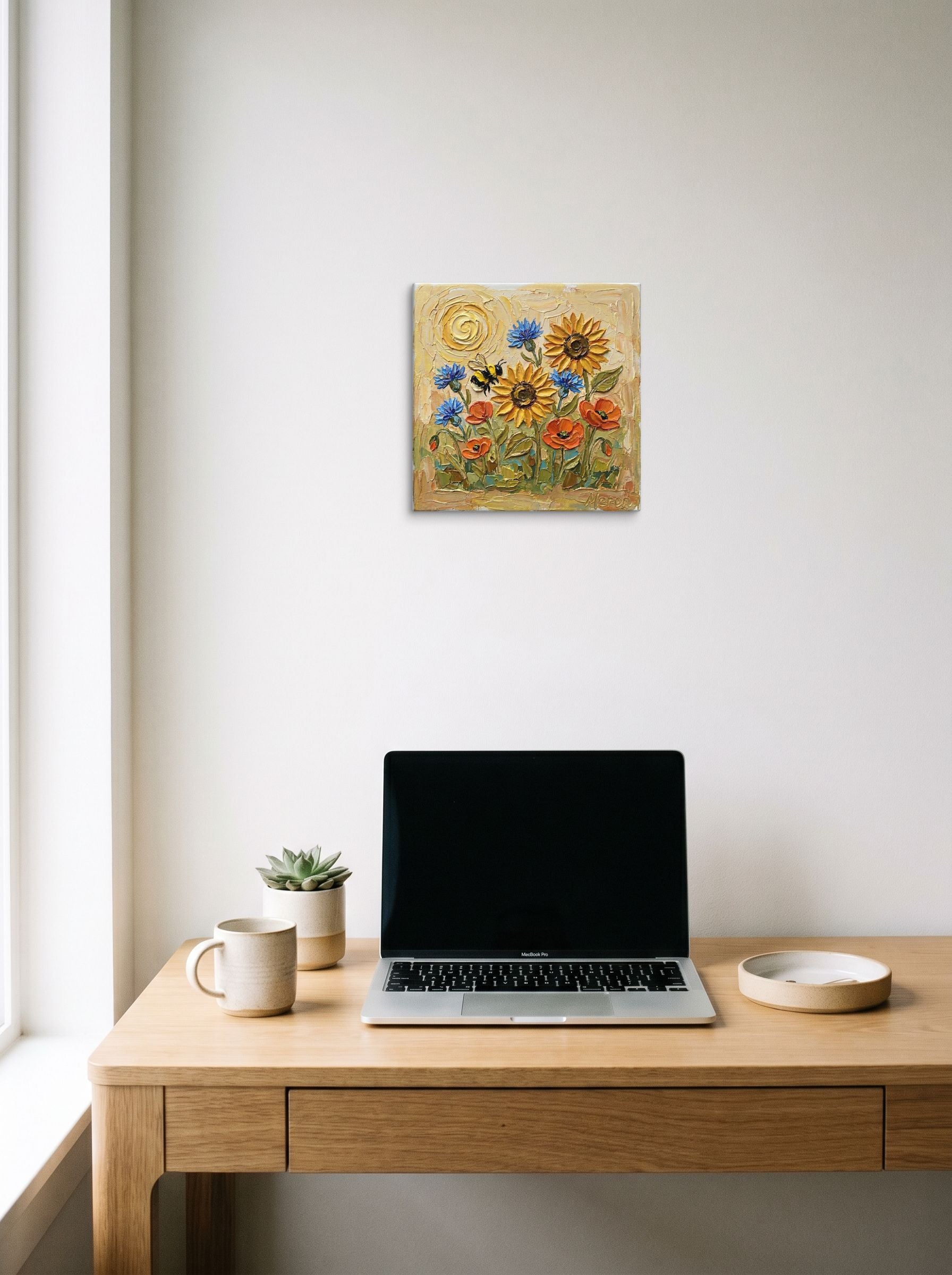 A 12x12 inch canvas Expressionism print of 'The Pollinator's Dance' hanging above a worktable with a laptop.