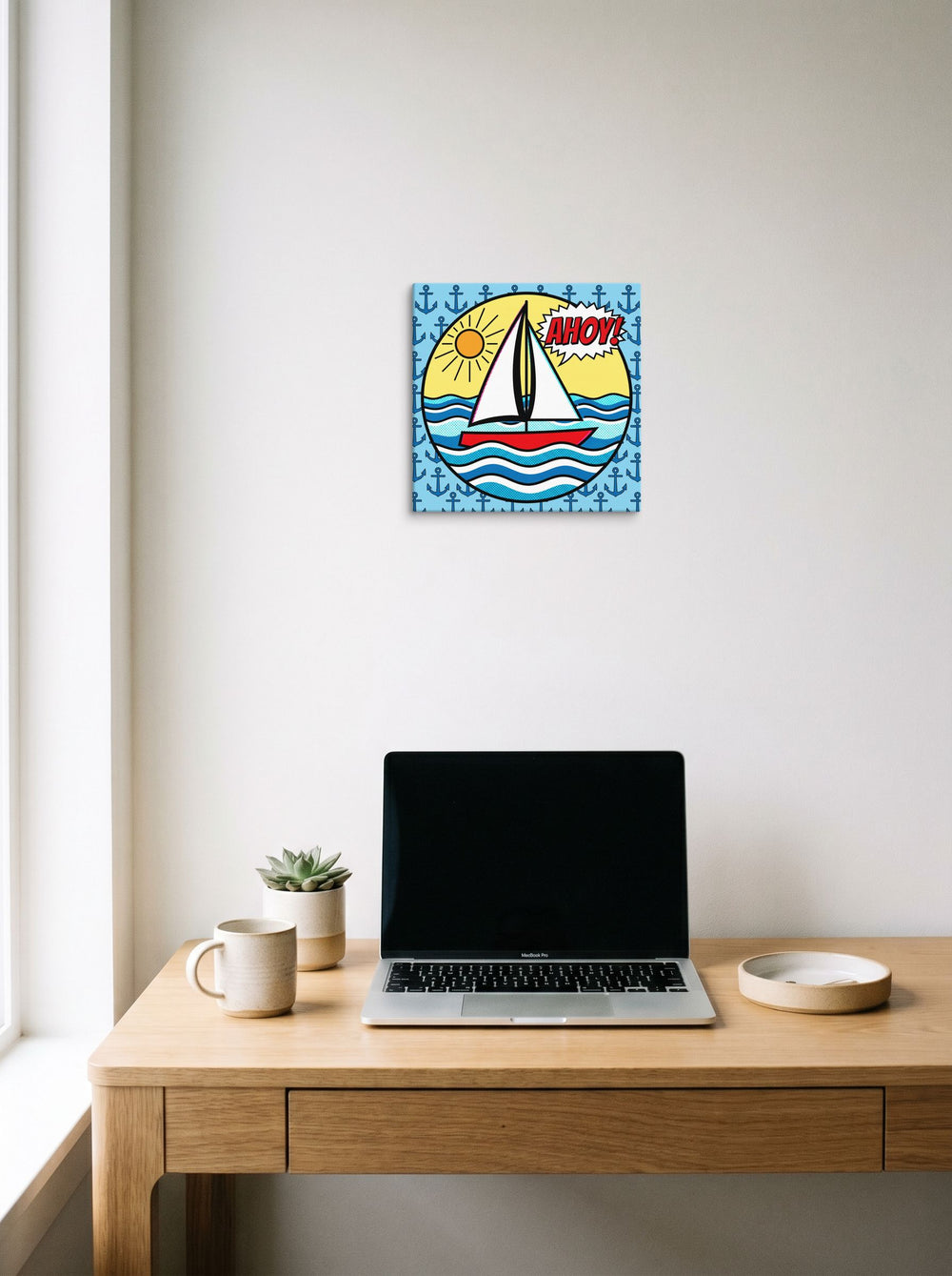 A 12x12 inch canvas Pop art print of 'Pop Art Ahoy' hanging above a worktable with a laptop.