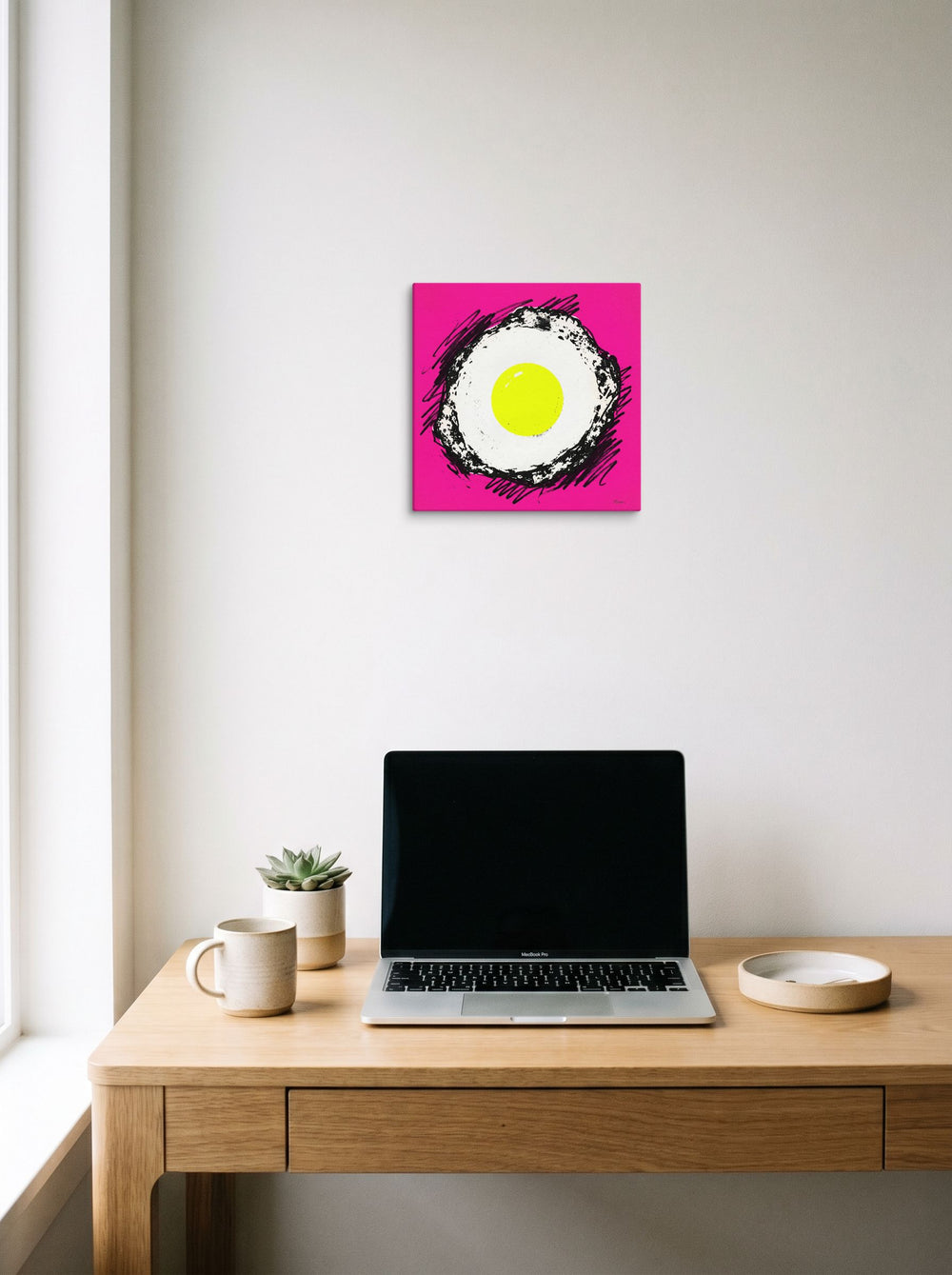 A 12x12 inch canvas Pop art print of 'Sunny Side Pop' hanging above a worktable with a laptop.