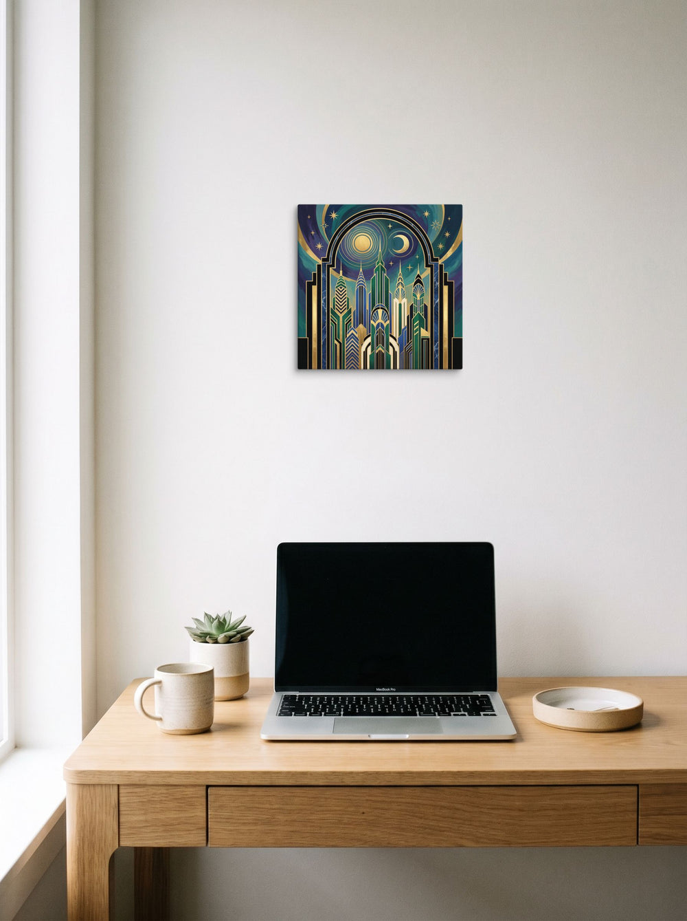 A 12x12 inch canvas Art Deco print of 'Midnight Metropolis' hanging above a worktable with a laptop.