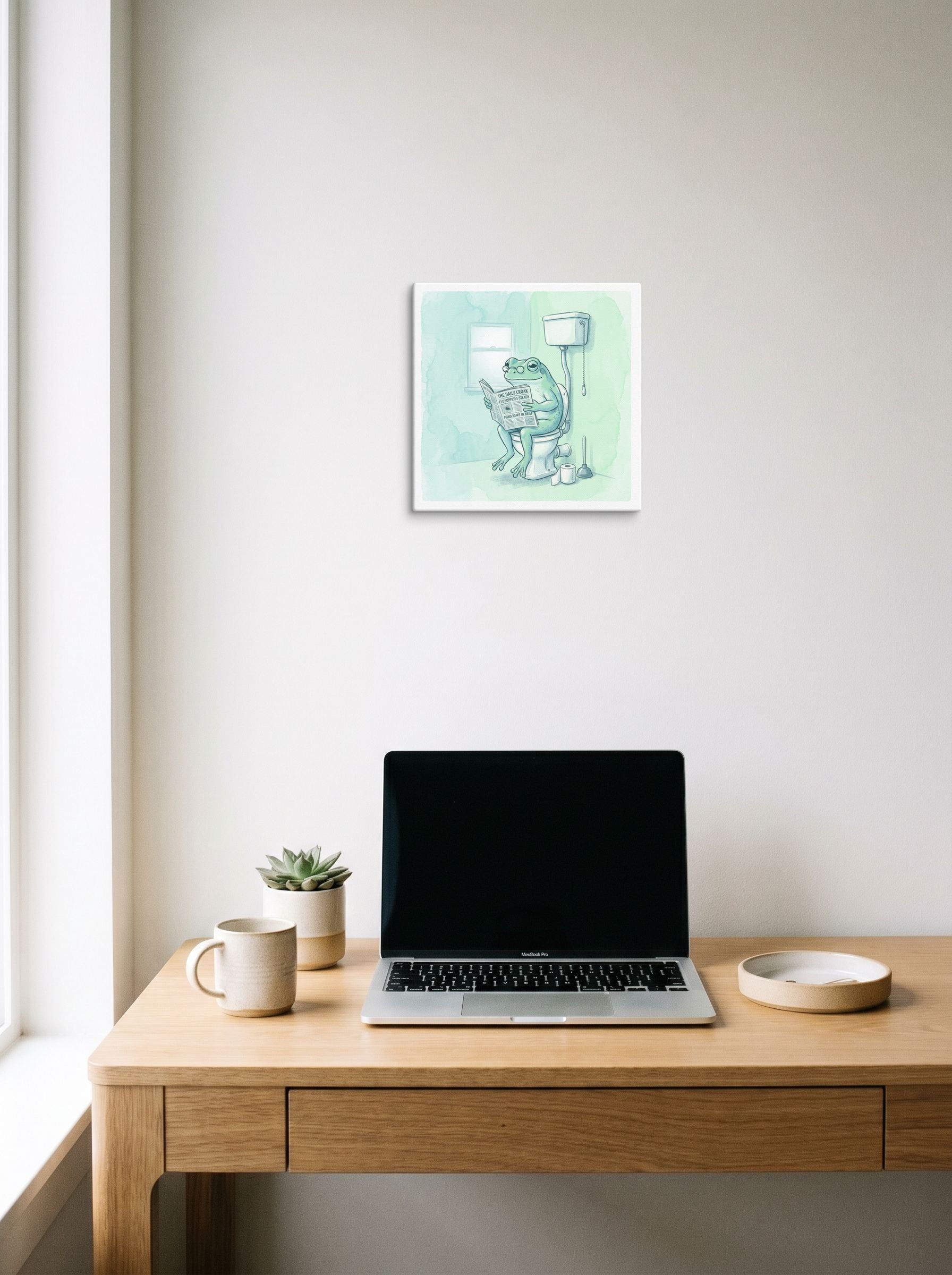 A 12x12 inch canvas Realism print of 'The Daily Croak' hanging above a worktable with a laptop.