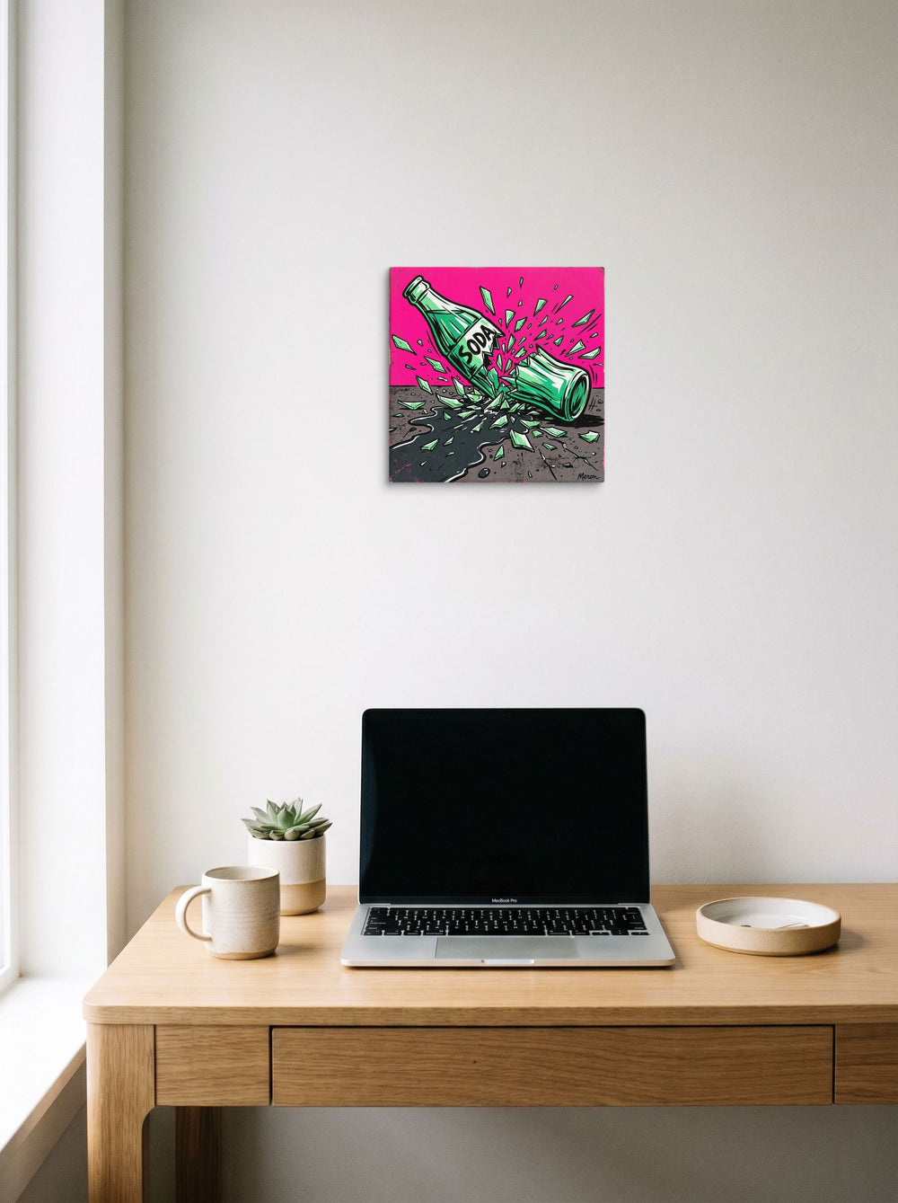 A 12x12 inch canvas Pop art print of 'Shattered Soda' hanging above a worktable with a laptop.