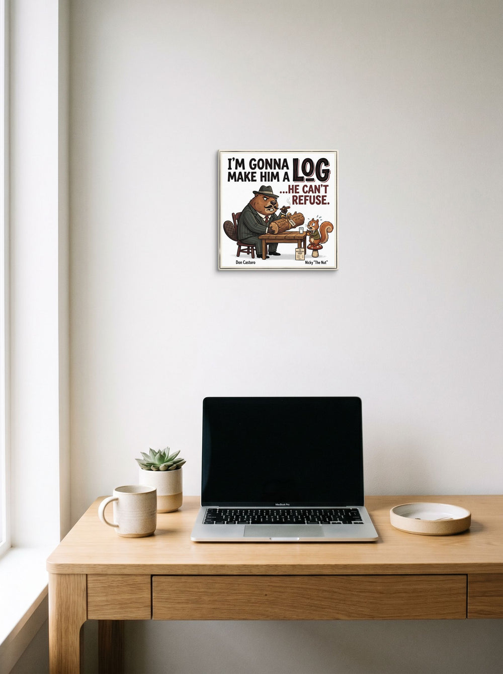 A 12x12 inch canvas Pop art print of 'Make Him a Log' hanging above a worktable with a laptop.