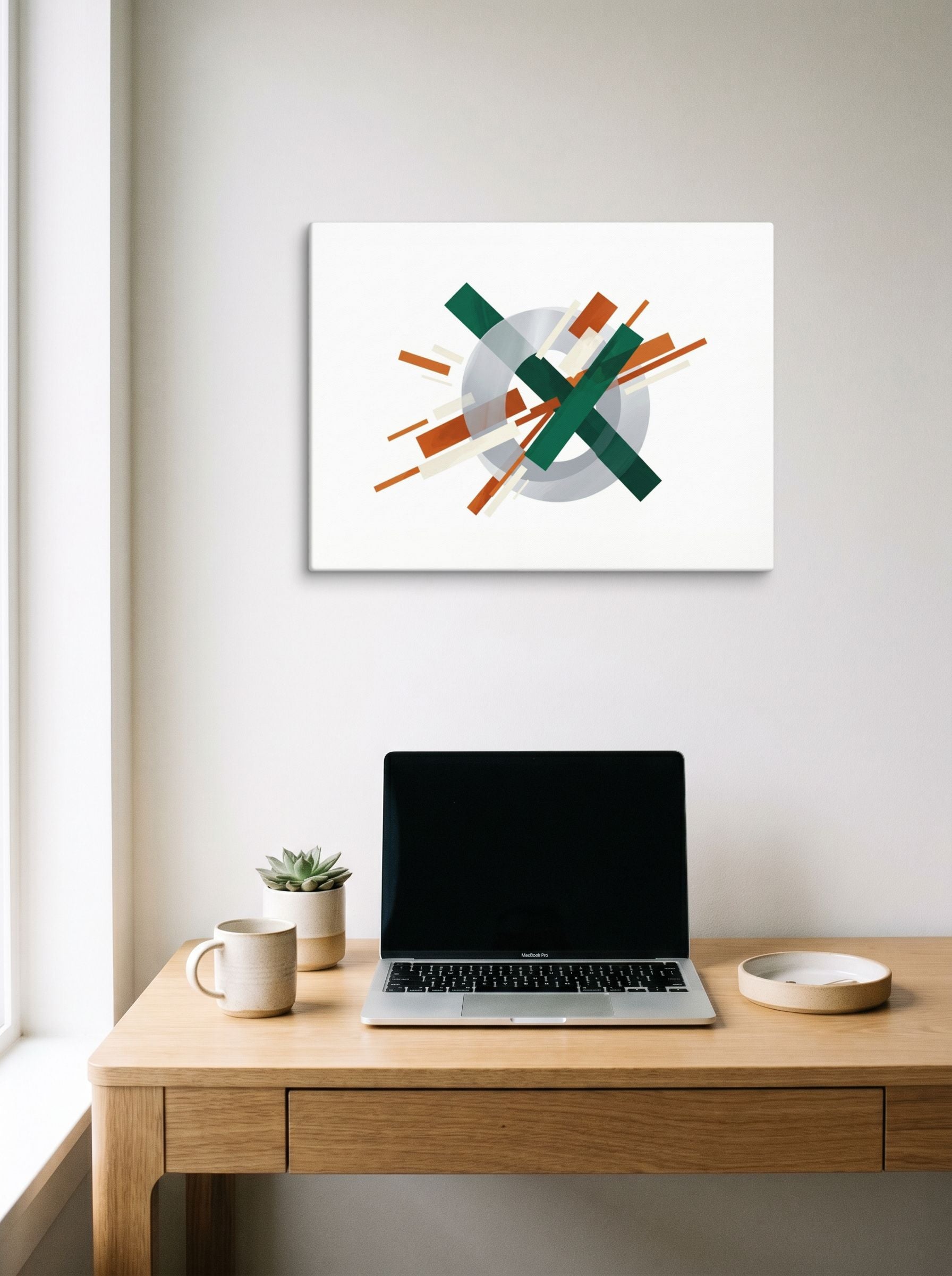A 24x18 inch canvas Suprematism print of 'Intersecting Perspectives' hanging above a worktable with a laptop.