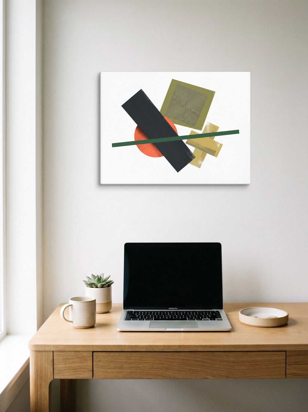 A 24x18 inch canvas Suprematism print of 'The Geometry of Sound' hanging above a worktable with a laptop.