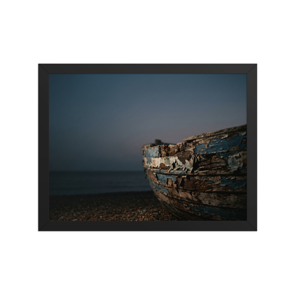 'The Faded Blue Boat' — a Art photography print. Close-up photograph of a weathered wooden boat with peeling blue paint resting on a rocky beach at dusk, suitable for a serene bathroom or living room.