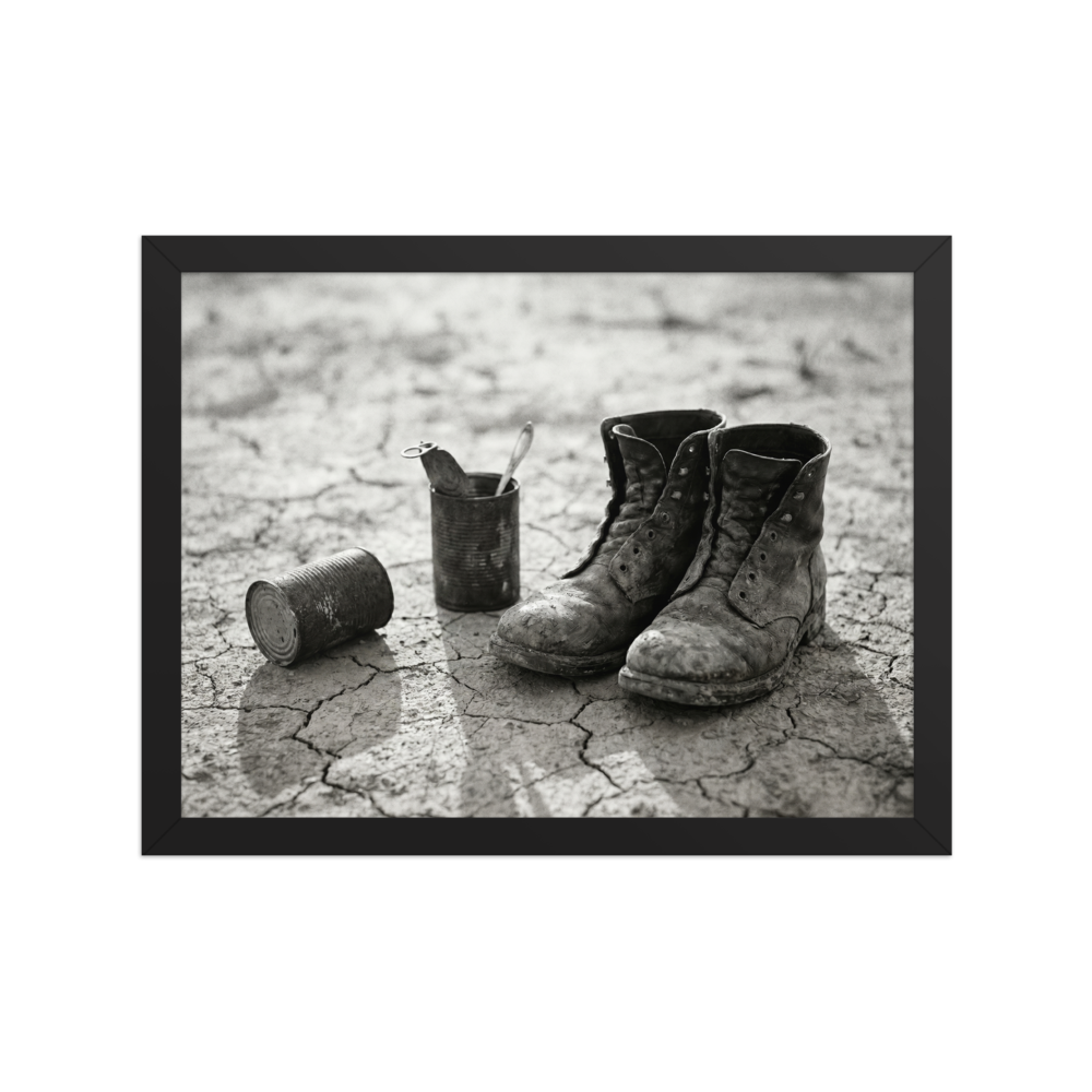 'The Drifter's Boots' — a American realism print. A black and white photograph of old, worn leather boots resting on cracked earth next to tin cans, perfect for a rustic Living Room.