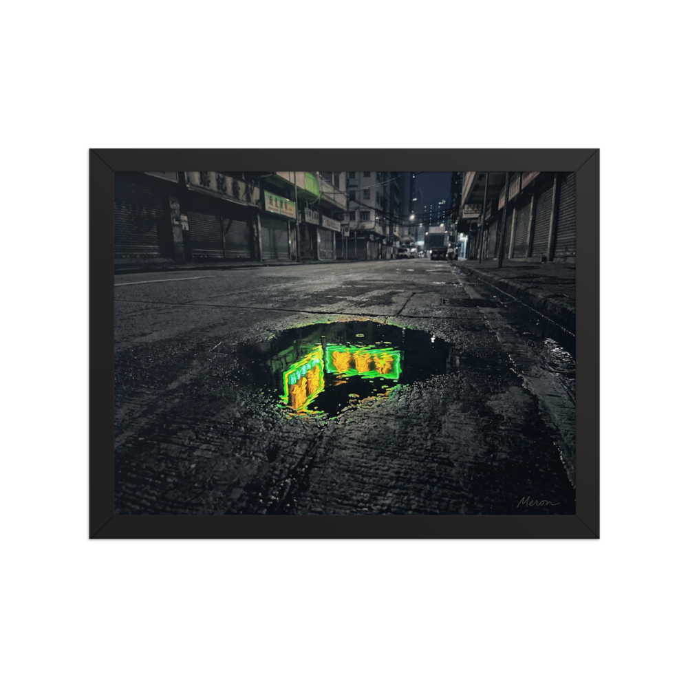 'Neon Puddle' — a Photorealism,Street art print. A dark, empty city street with closed shutters features a puddle in the foreground reflecting a bright green and yellow neon sign, perfect for a modern office or man cave.