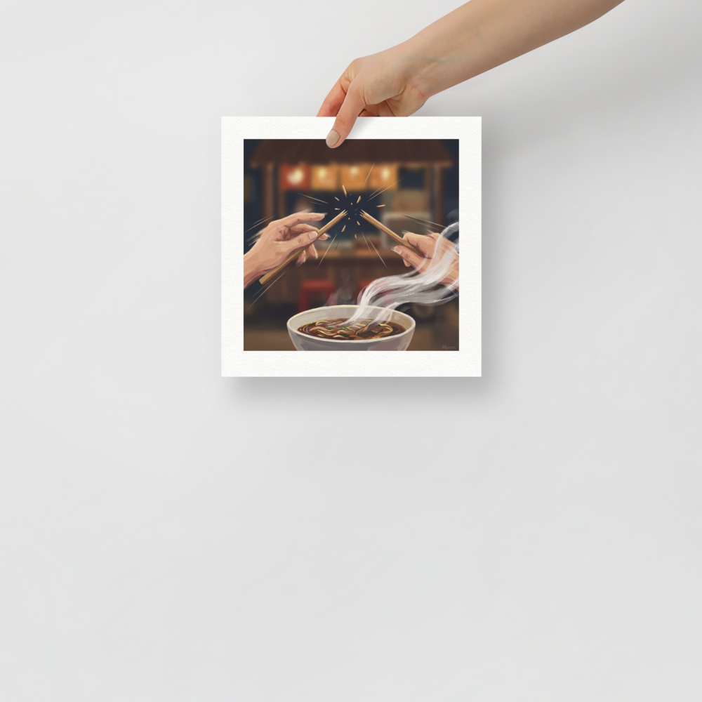 Hands snapping chopsticks in half above a steaming bowl of Japanese ramen noodles in a cozy kitchen. Available as the Digital art art print 'The Chopstick Snap'.
