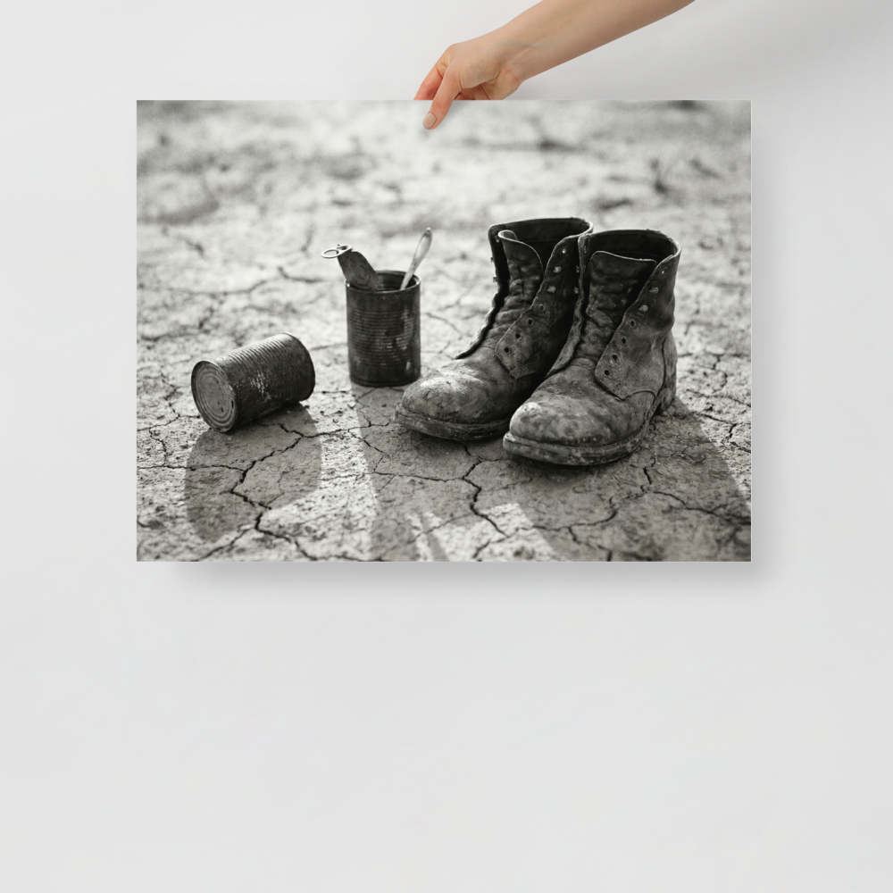 'The Drifter's Boots' — a American realism print. A black and white photograph of old, worn leather boots resting on cracked earth next to tin cans, perfect for a rustic Living Room.
