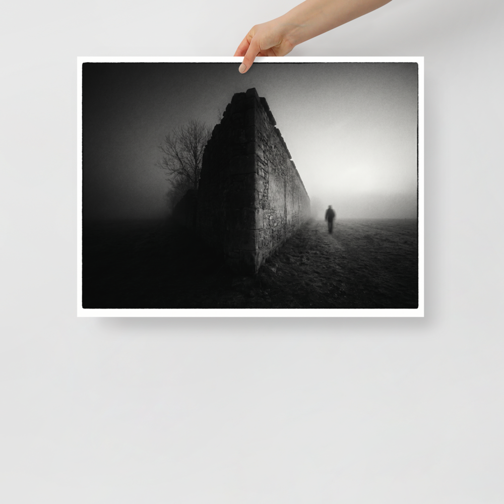 'Echoes in the Mist' — a Art photography print. A moody black and white photograph of a lone figure walking into dense fog next to an old stone wall, ideal for a modern Office or Den.