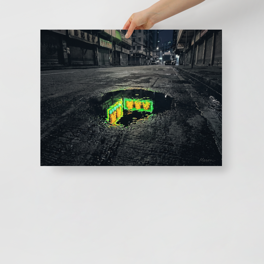 'Neon Puddle' — a Photorealism,Street art print. A dark, empty city street with closed shutters features a puddle in the foreground reflecting a bright green and yellow neon sign, perfect for a modern office or man cave.