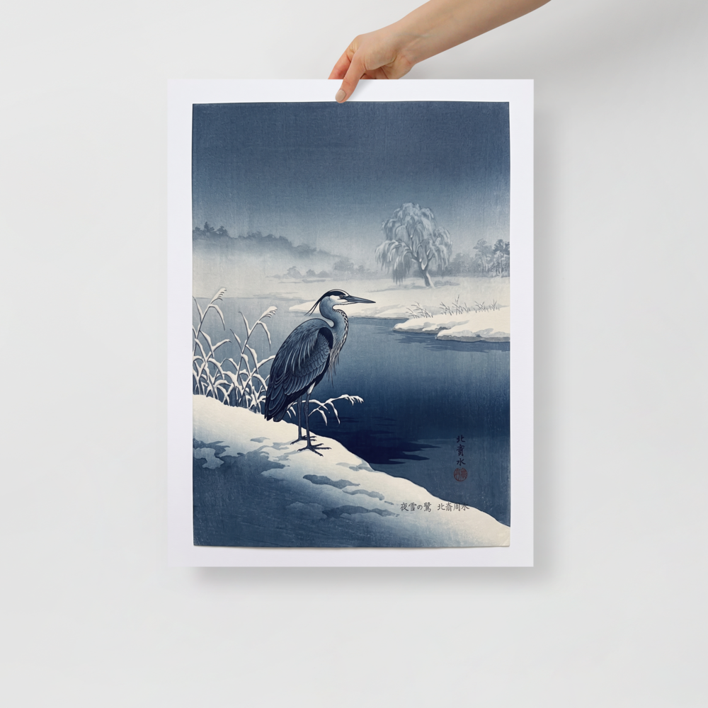 'Winter Heron' — a Shin hanga print. A stately blue heron stands on a snow-covered riverbank along dark winter waters, bringing a serene atmosphere to a calm bedroom.