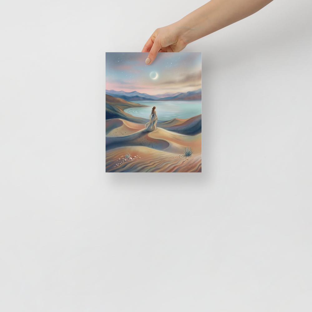 'Desert Moonrise' — a Magic realism print. A woman in a flowing dress standing on rolling sand dunes looking over a turquoise bay toward mountains under a twilight sky with a crescent moon.