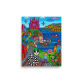 'Checkered Cat's Castle Dream' — a Naive art print. A colorful naive art scene featuring a black and white checkered cat sitting on a patterned rug in a playroom, with a seaside village and pink castle in the background.