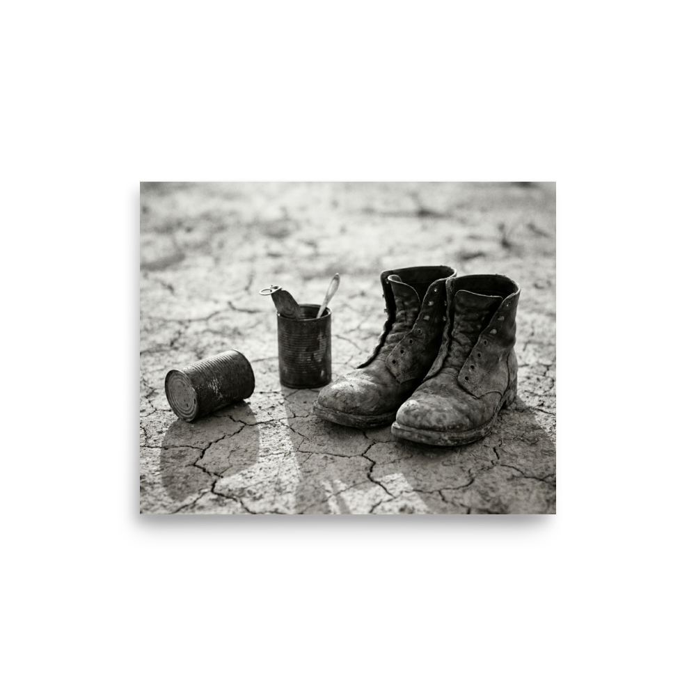 'The Drifter's Boots' — a American realism print. A black and white photograph of old, worn leather boots resting on cracked earth next to tin cans, perfect for a rustic Living Room.