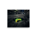 'Neon Puddle' — a Photorealism,Street art print. A dark, empty city street with closed shutters features a puddle in the foreground reflecting a bright green and yellow neon sign, perfect for a modern office or man cave.