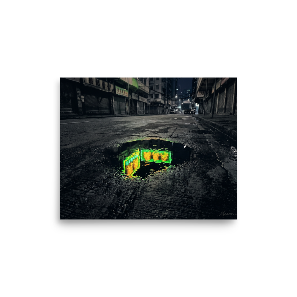 'Neon Puddle' — a Photorealism,Street art print. A dark, empty city street with closed shutters features a puddle in the foreground reflecting a bright green and yellow neon sign, perfect for a modern office or man cave.