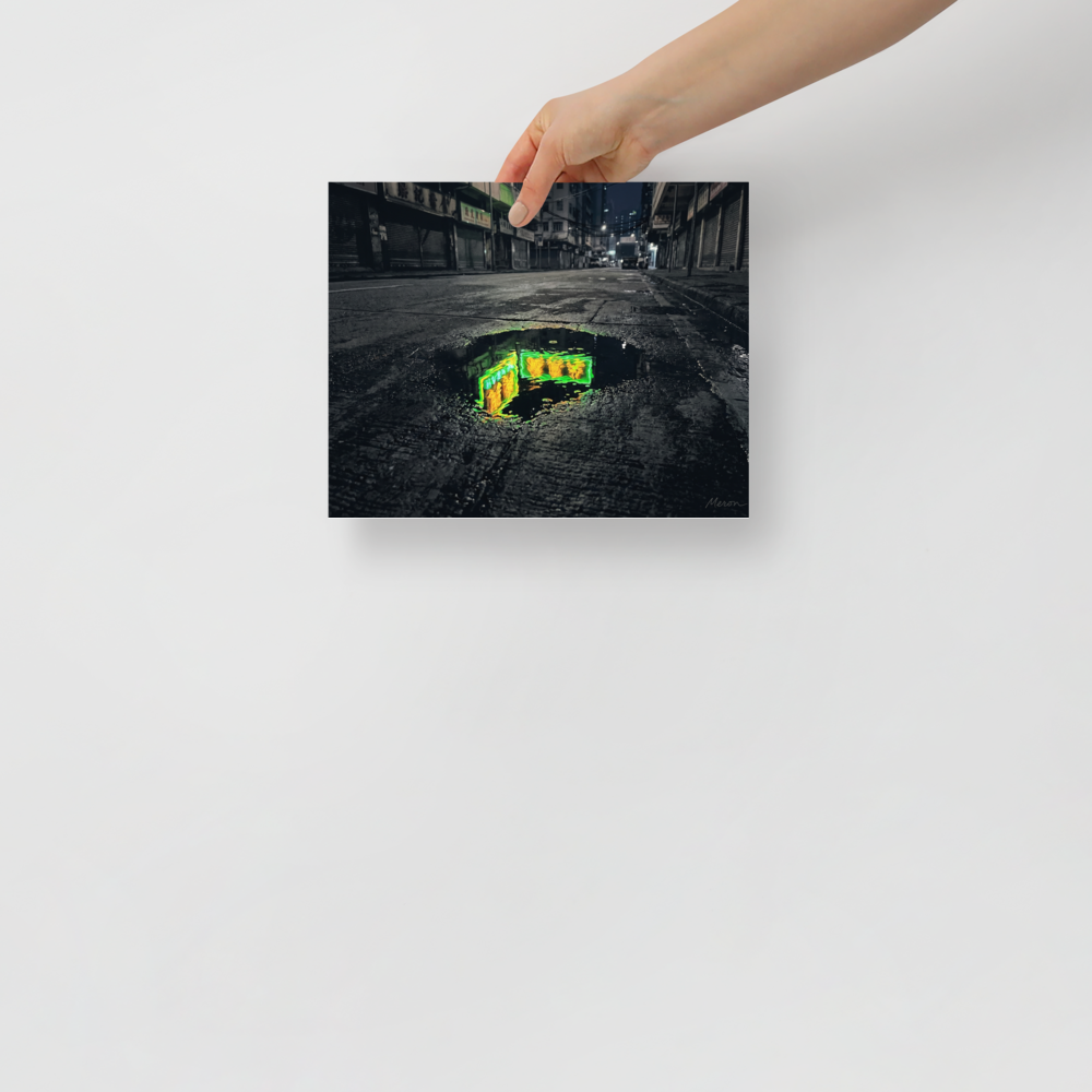 'Neon Puddle' — a Photorealism,Street art print. A dark, empty city street with closed shutters features a puddle in the foreground reflecting a bright green and yellow neon sign, perfect for a modern office or man cave.