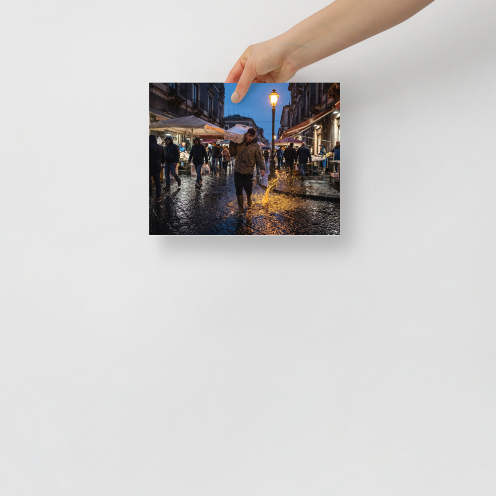 'Market Rain at Dusk' — a Art photography print. Market worker carrying a fish crate splashing through rainy wet cobblestones under a glowing streetlamp at dusk, atmospheric street photography.
