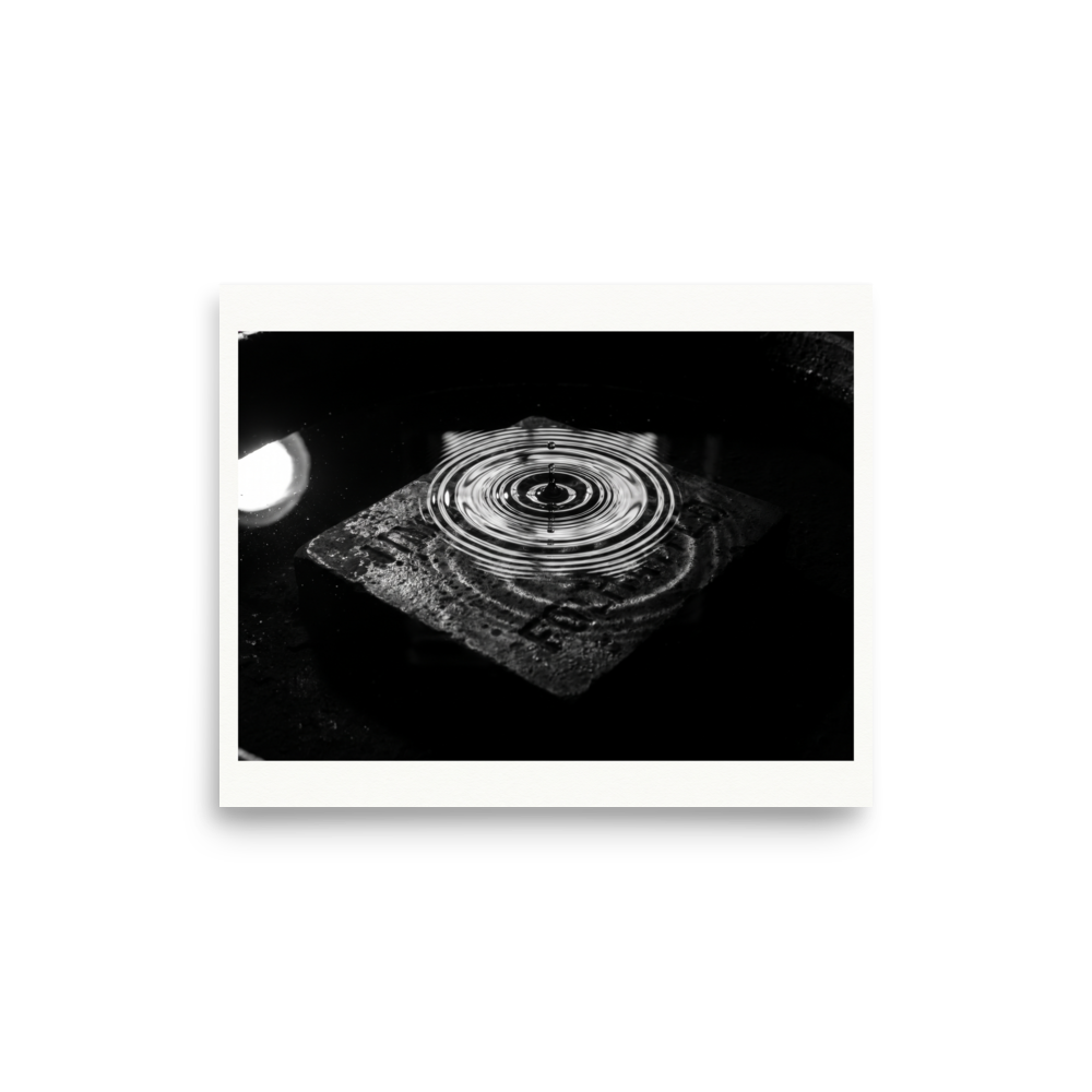 'Concentric Resonance' — a Art photography print. A dramatic black and white photograph capturing concentric water ripples above a textured stone, well suited for a modern office or living room.