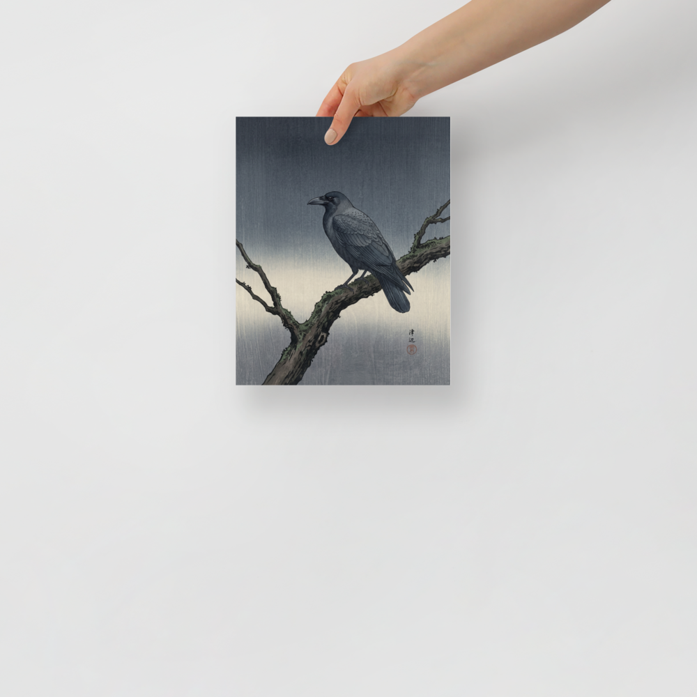 'Solitary Raven at Dusk' — a Shin hanga print. A dark raven perches on a mossy winter branch against a textured gray woodblock background, bringing a calm aesthetic to an office.