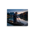 'Twilight River' — a Art photography print. A fisherman gathers his net on a calm river at dusk with illuminated waterfront buildings, creating a serene mood suited for an office.