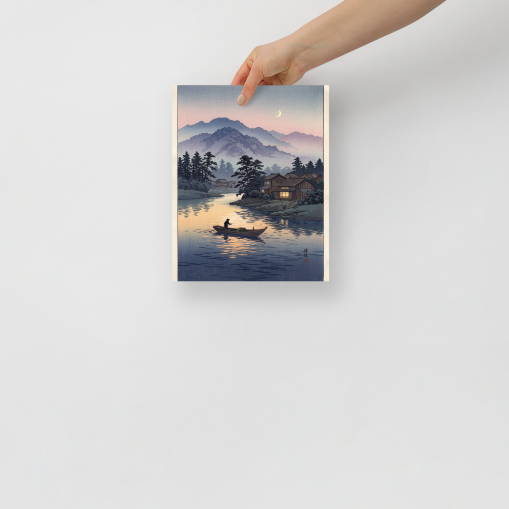 'Moonlit River Crossing' — a Shin hanga print. A lone boatman rows across a calm river reflecting twilight colors and warm cabin window light beneath misty mountains, perfect for a living room.