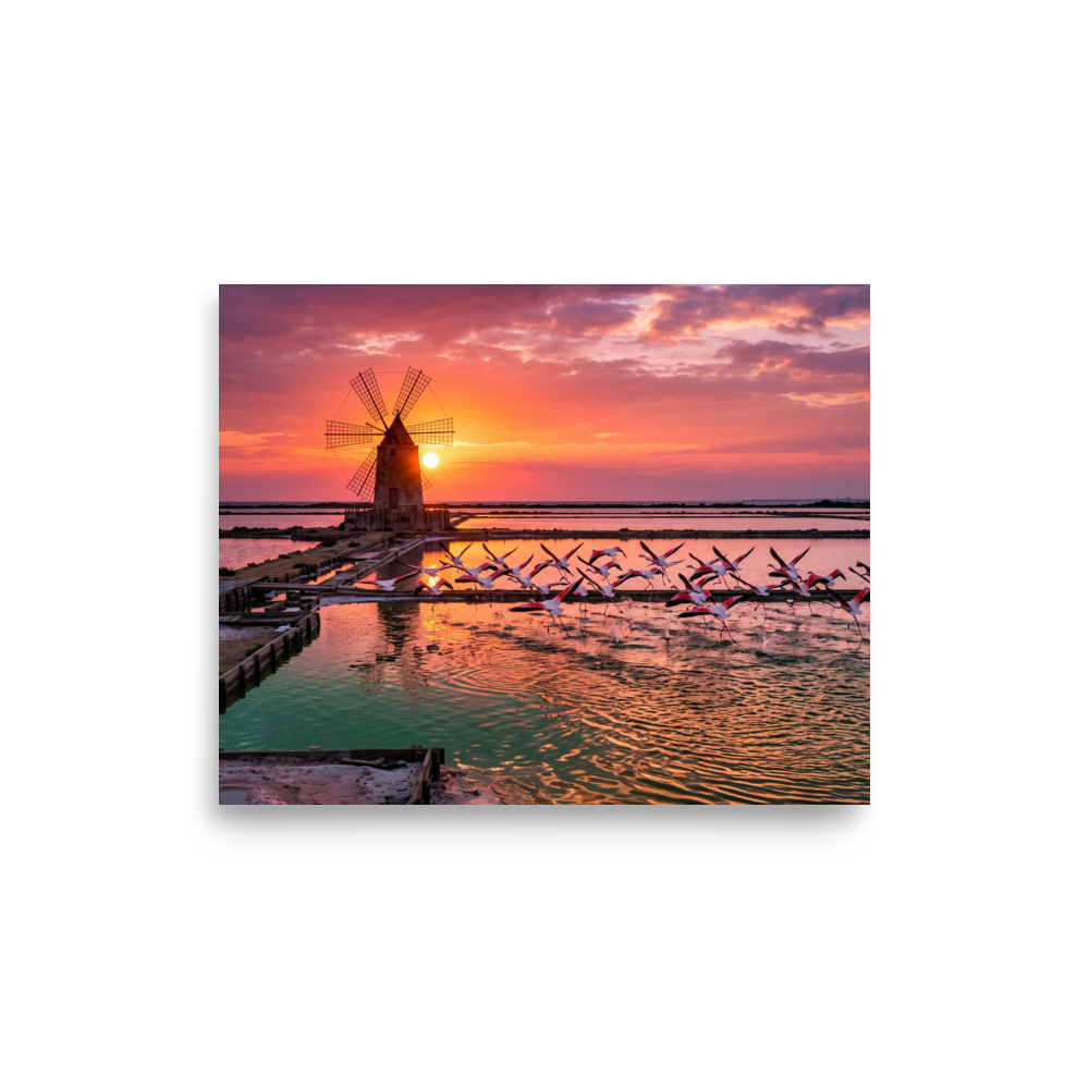 'Flamingos at Dusk' by Meron. A breathtaking photograph of pink flamingos flying across tranquil salt pans at sunset near a traditional windmill, perfect for a peaceful bedroom or living room. A Art photography wall art print.