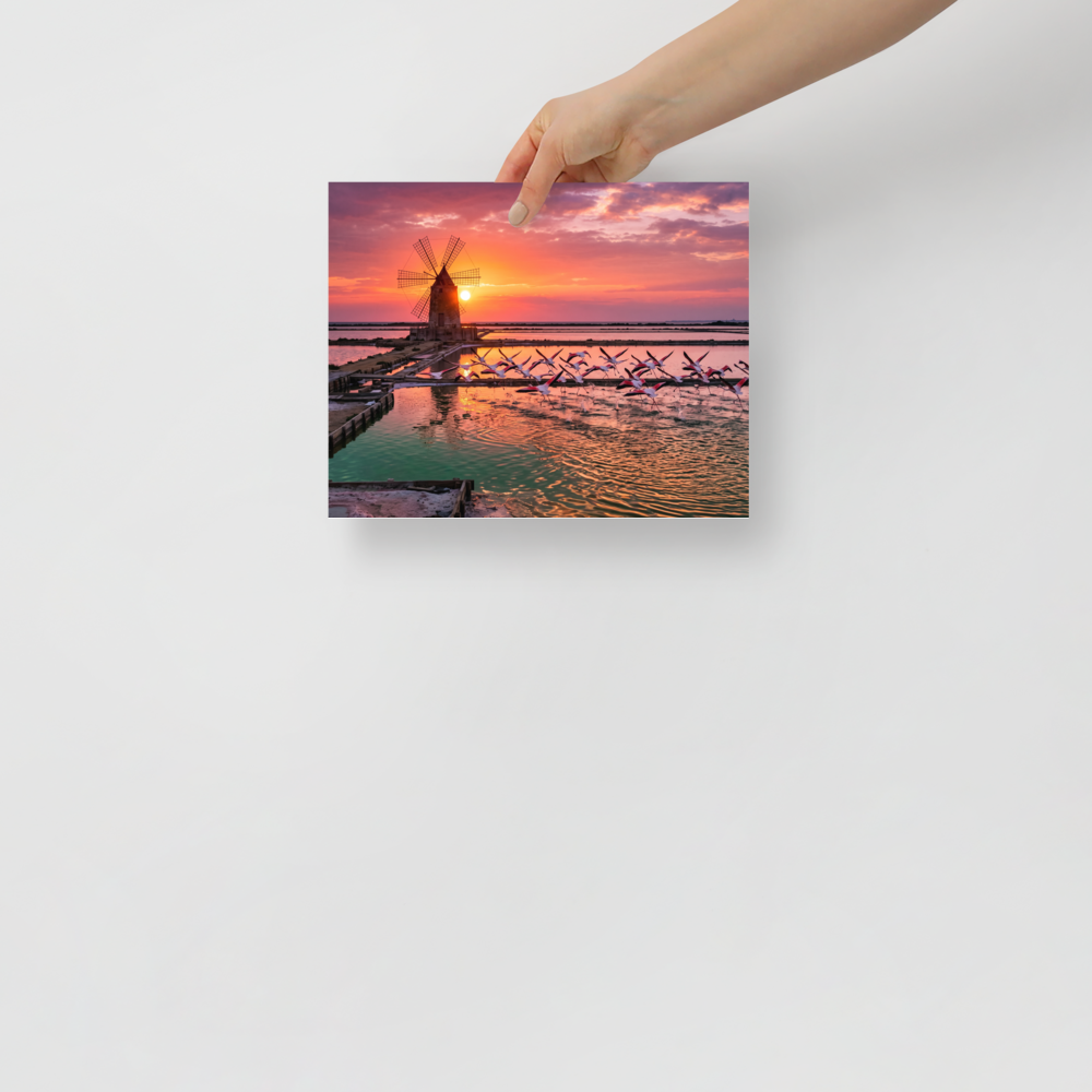 Art photography wall art exploring animals, 'Flamingos at Dusk'. A breathtaking photograph of pink flamingos flying across tranquil salt pans at sunset near a traditional windmill, perfect for a peaceful bedroom or living room.