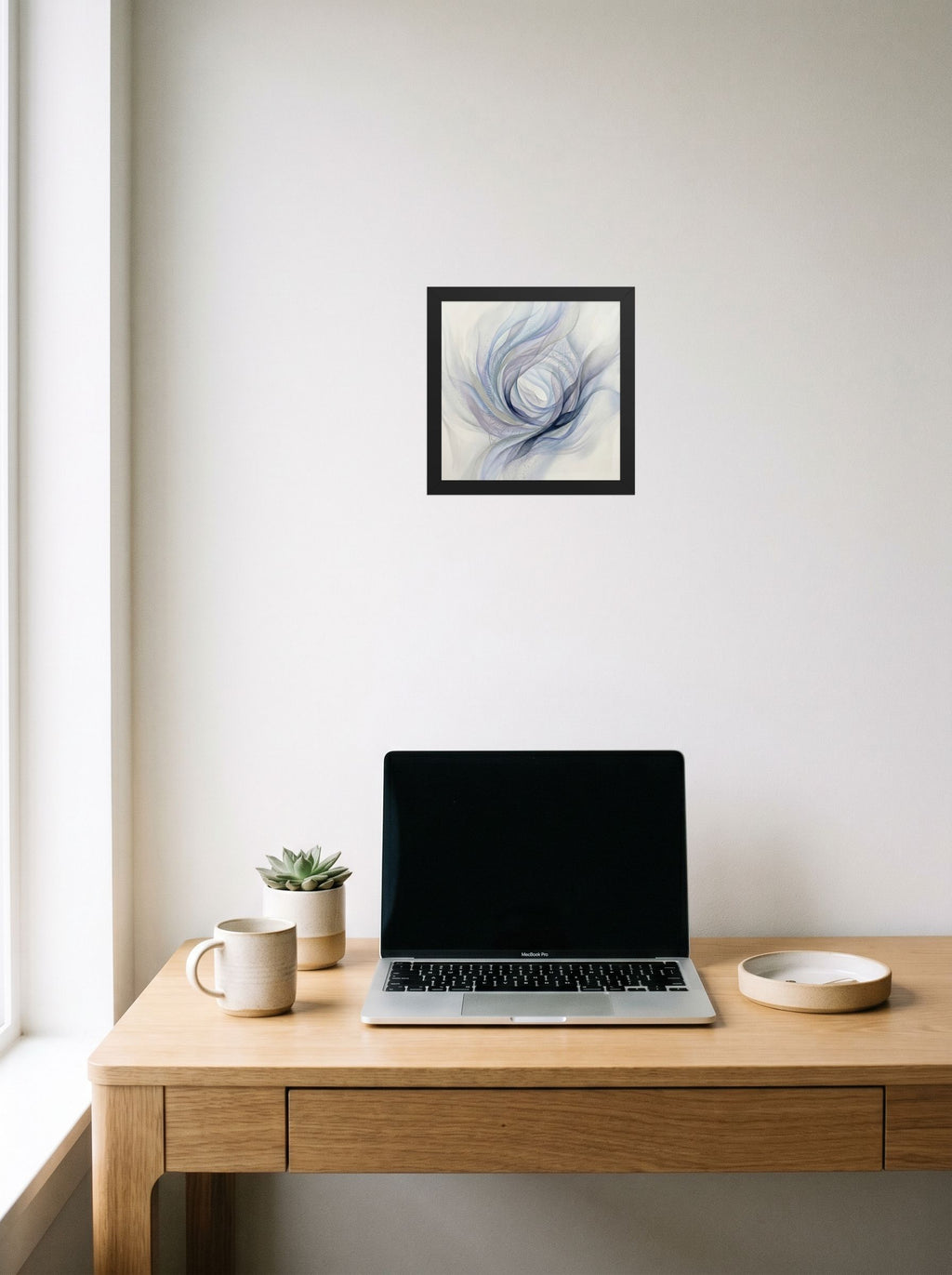 A 10x10 inch black framed Abstract art print of 'Ethereal Whispers in the Vortex' hanging above a worktable with a laptop.