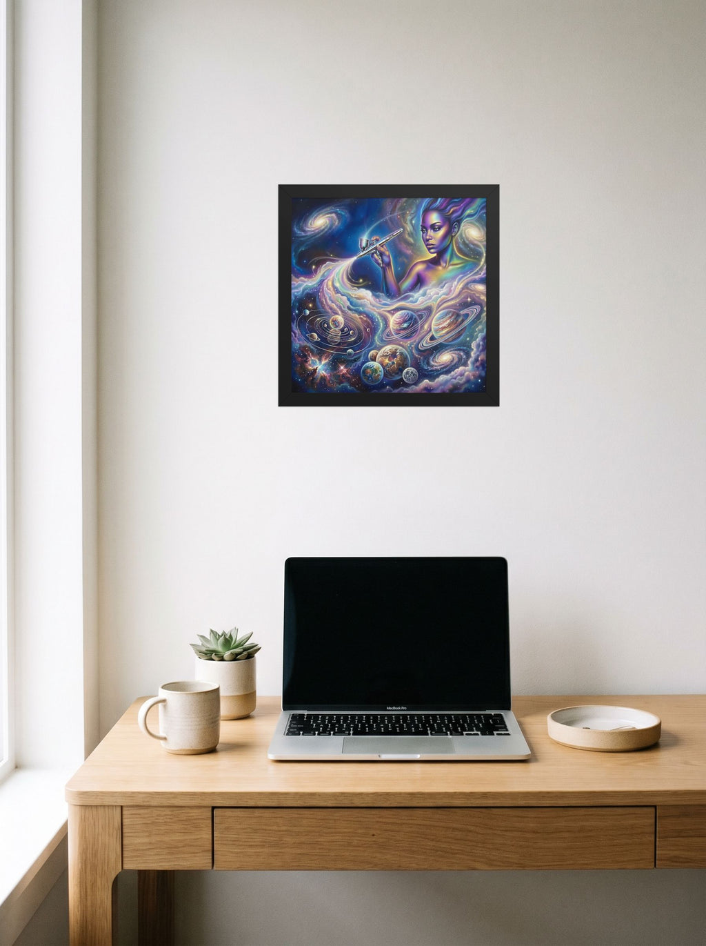 A 12x12 inch black framed Space art print of 'The Cosmic Painter' hanging above a worktable with a laptop.