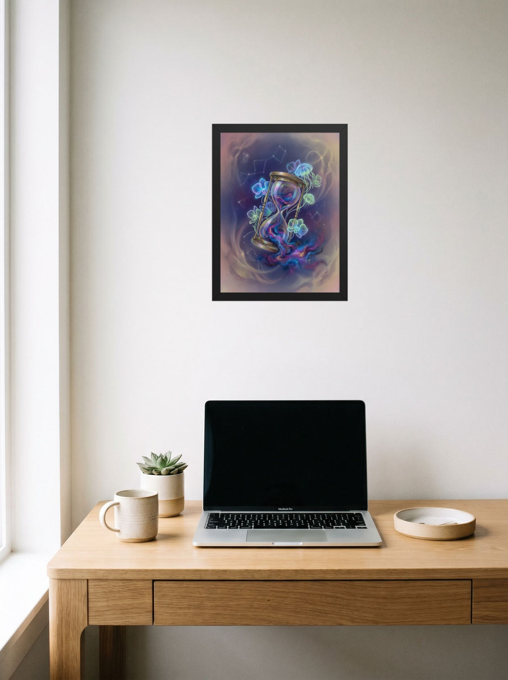 A 12x16 inch black framed Magic realism print of 'Sands of the Nebula' hanging above a worktable with a laptop.