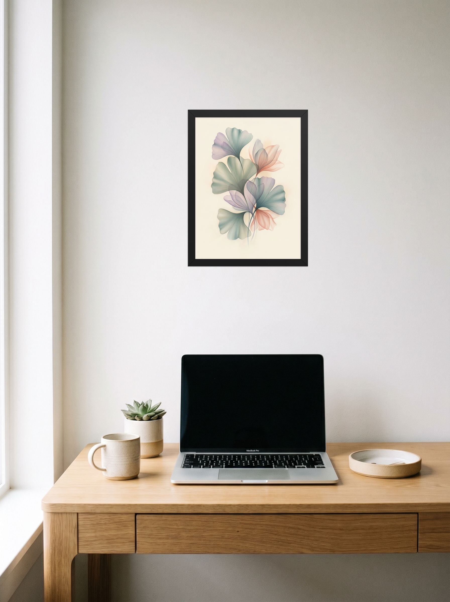 A 12x16 inch black framed Abstract art print of 'Ethereal Ginkgo Whispers' hanging above a worktable with a laptop.