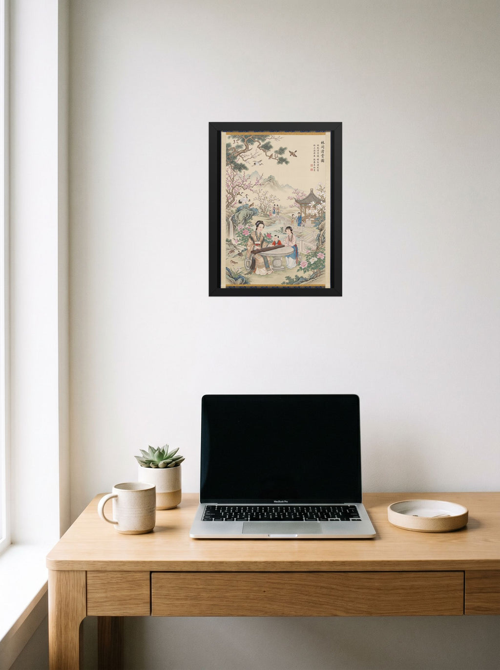A 12x16 inch black framed Fine Art print of 'Melody in the Spring Garden' hanging above a worktable with a laptop.