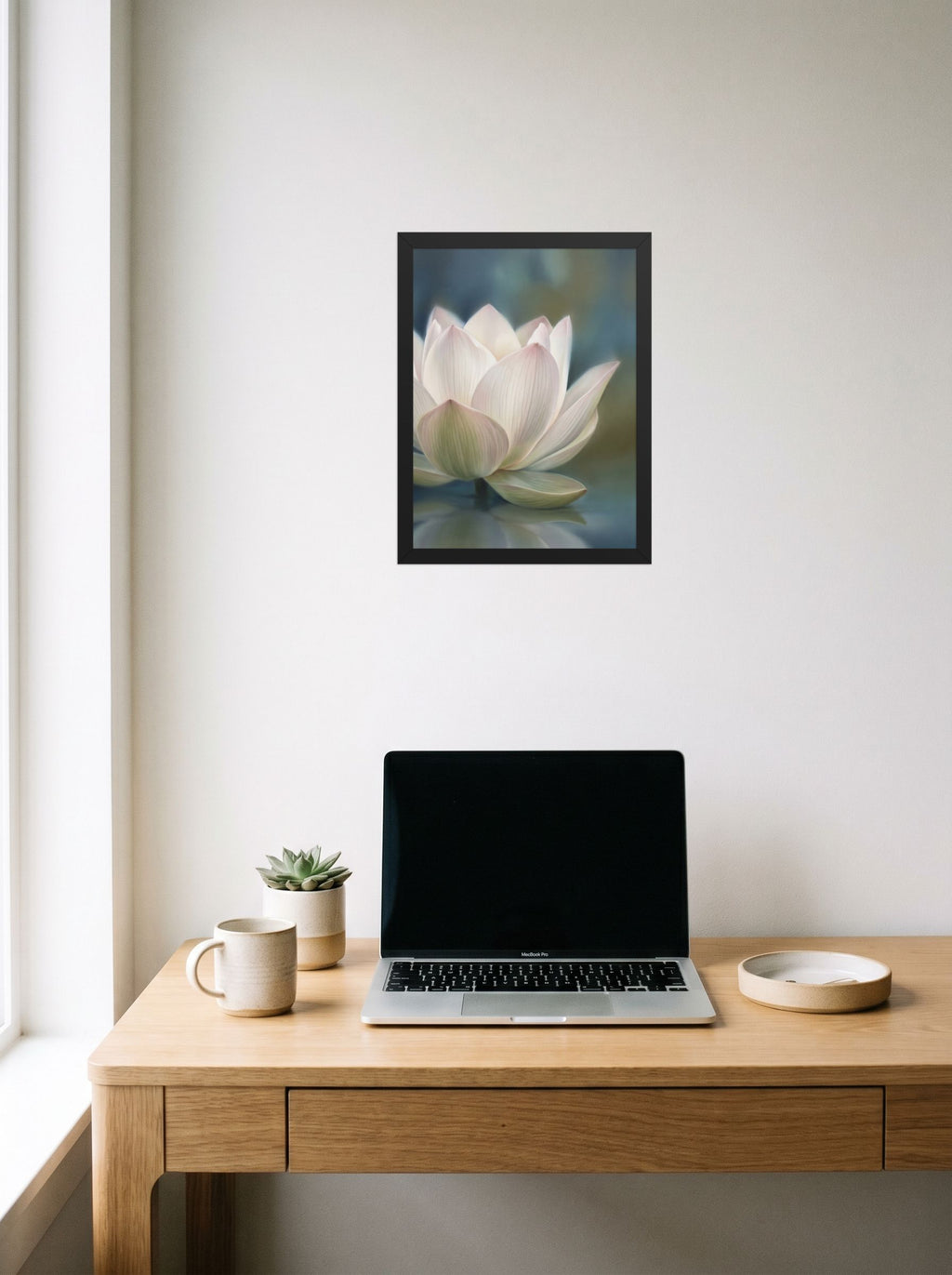 A 12x16 inch black framed Realism print of 'Serene Lotus Reflection' hanging above a worktable with a laptop.