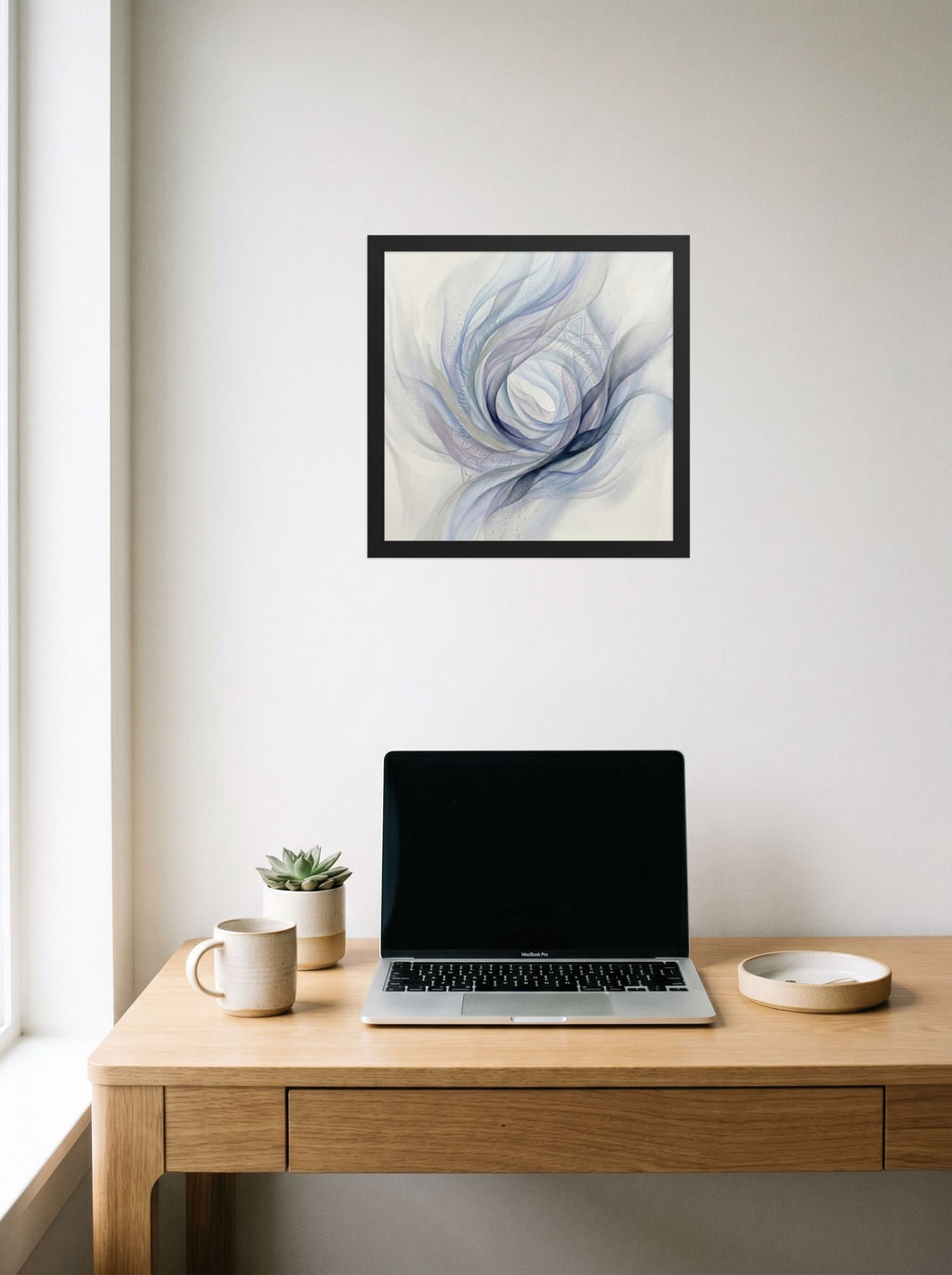 A 14x14 inch black framed Abstract art print of 'Ethereal Whispers in the Vortex' hanging above a worktable with a laptop.